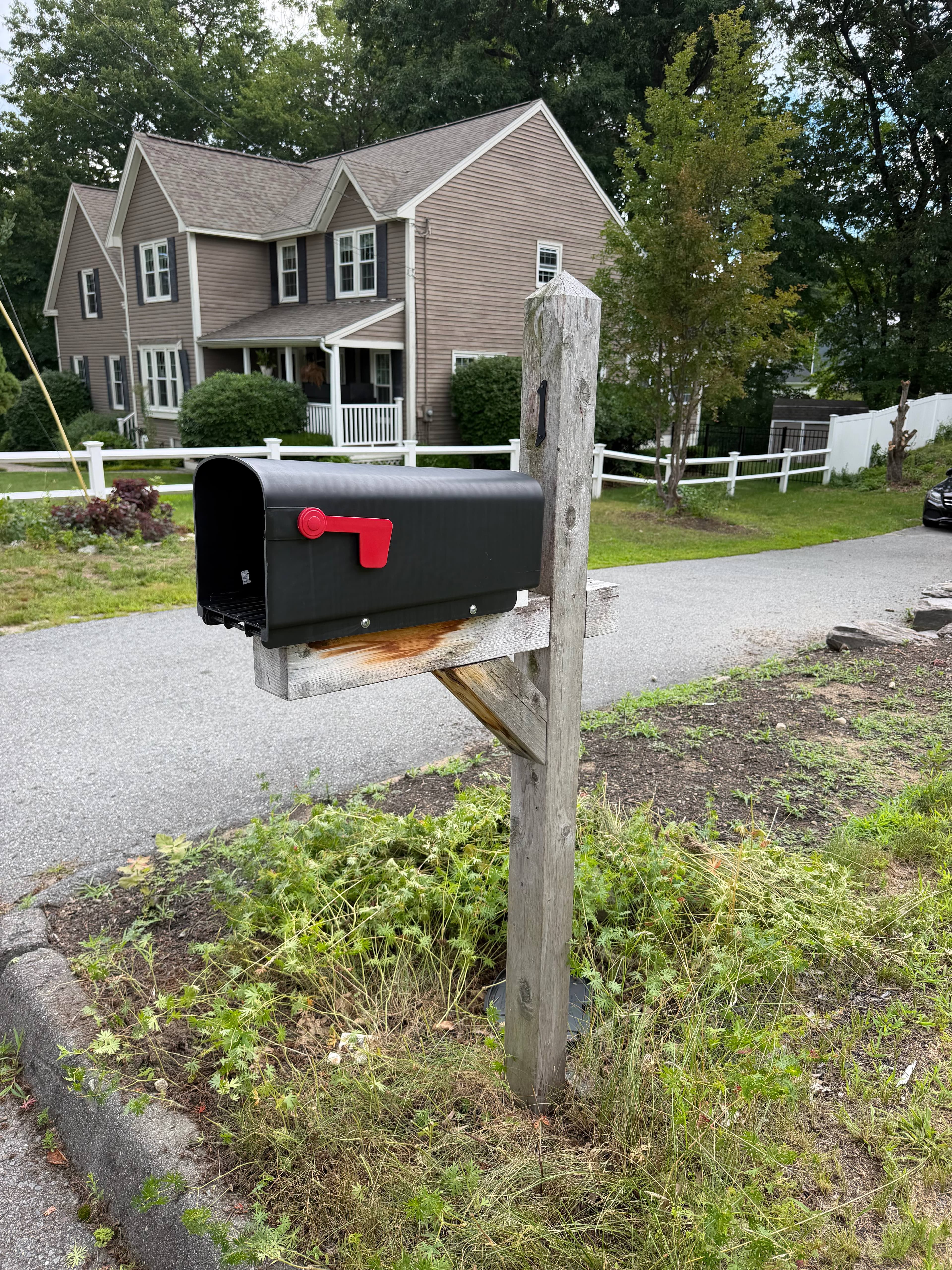 Before: Weathered gray wood mailbox post surrounded by overgrown weeds